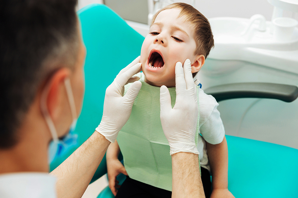 Dentist examining teeth of little boy witting with mouth opened Odontopediatria